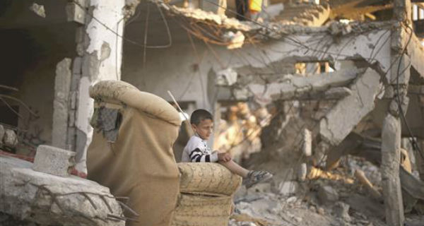 طفل فلسطيني يجلس خارج منزله المدمر في غزة امس (رويترز)
