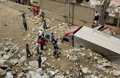 أشخاص ينظرون إلى شاحنة علقت في الطين بعد وقوع انجراف صخري في بيرو