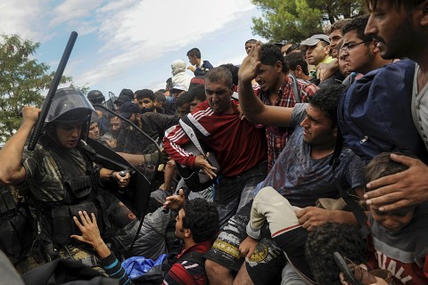 شرطي مقدوني يرفع عصاه في وجه اللاجئين لمنعهم من عبور الحدود اليونانية المقدونية