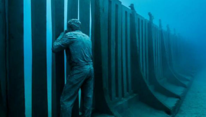 تمثال بجانب الجدار الكبير الذي يزن 100 طن تحت الماء في متحف "أتلانتيكو" في أوروبا.