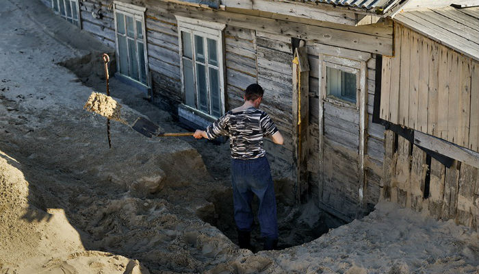 أحد الرجال يزيل الرمال من أمام باب منزله في قرية "شوينا" في روسيا.