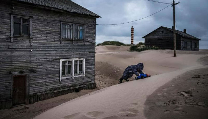 فتاة تلعب بجانب منزل في "شوينا" الغارقة بالرمال في روسيا.