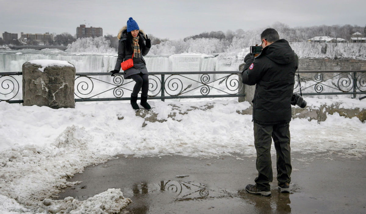 شاب يلتقط صورة لفتاة بجوار شلالات نياجرا المتجمدة في كندا.