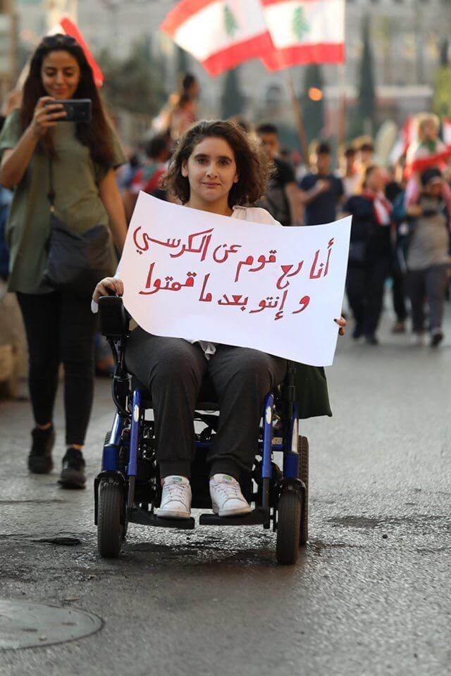 صورة لفتاة مقعدة في الاحتجاجات تحمل شعاراً مؤثراً