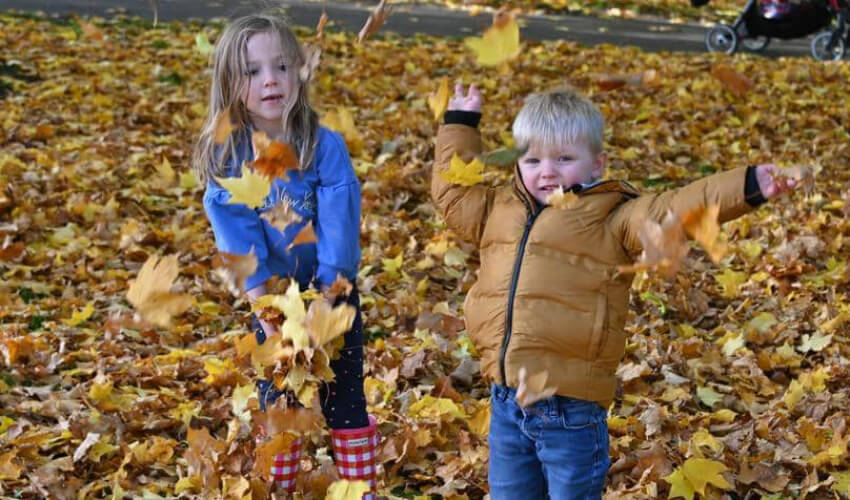 طفلان من غلاسكو في اسكتلندا يستمتعان بأوراق الخريف بجانب إحدى البحيرات.