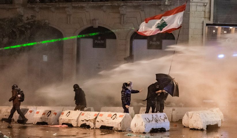 متظاهرون يحملون العلم اللبناني في مواجهة خراطيم المياه