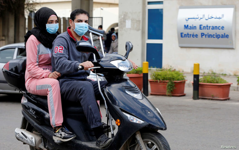 إمرأة ورجل يرتديان الكمامات للوقاية من فيروس كورونا على دراجة نارية امام مستشفى رفيق الحريري الجامعي (رويترز)