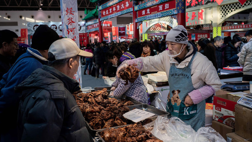 عمال يرتدون أقنعة للوجه يقومون بالشواء في سوق في ووهان بمقاطعة هوبي بوسط الصين (أ.ف.ب)