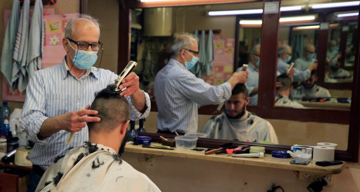 حلاق يرتدي قناعًا وقائيًا للوقاية من فيروس كورونا في لبنان يحلق رأس أحد العملاء في محلة في صيدا (رويترز/علي حشيشو)