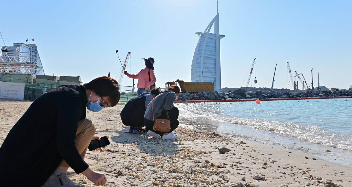 سياح يرتدون كمامات يبحثون عن صدف على شاطئ بجوار برج العرب في دبي (AFP)