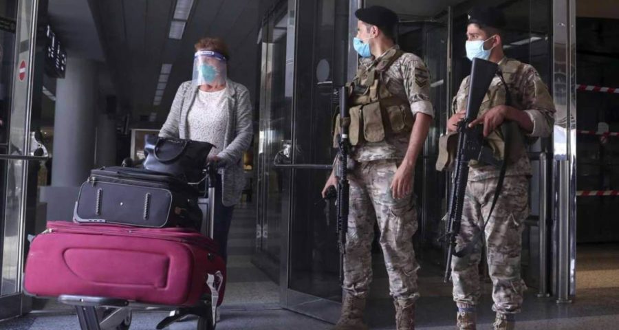 جنديان من الجيش اللبناني ينظران الى امراة آتية عبر مطار رفيق الحريري بعد فتحه مع استمرار انتشار فيروس كورونا في لبنان (أسوشييتد برس)