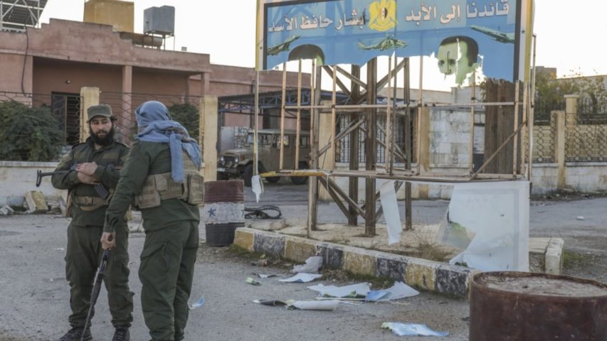 Syrian opposition fighters stand next to a government sign after entering the village of Anjara, western outskirts of Aleppo (AP)